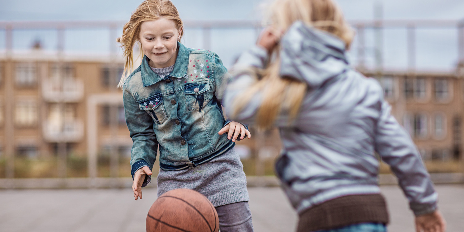 Two girls playing basketball outside.