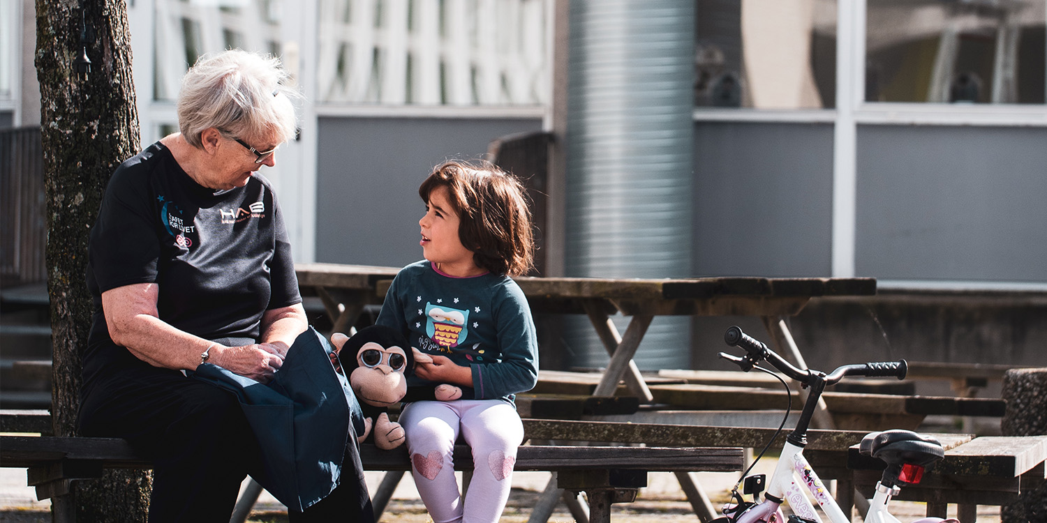 Child talking to an older woman on a bench outside.