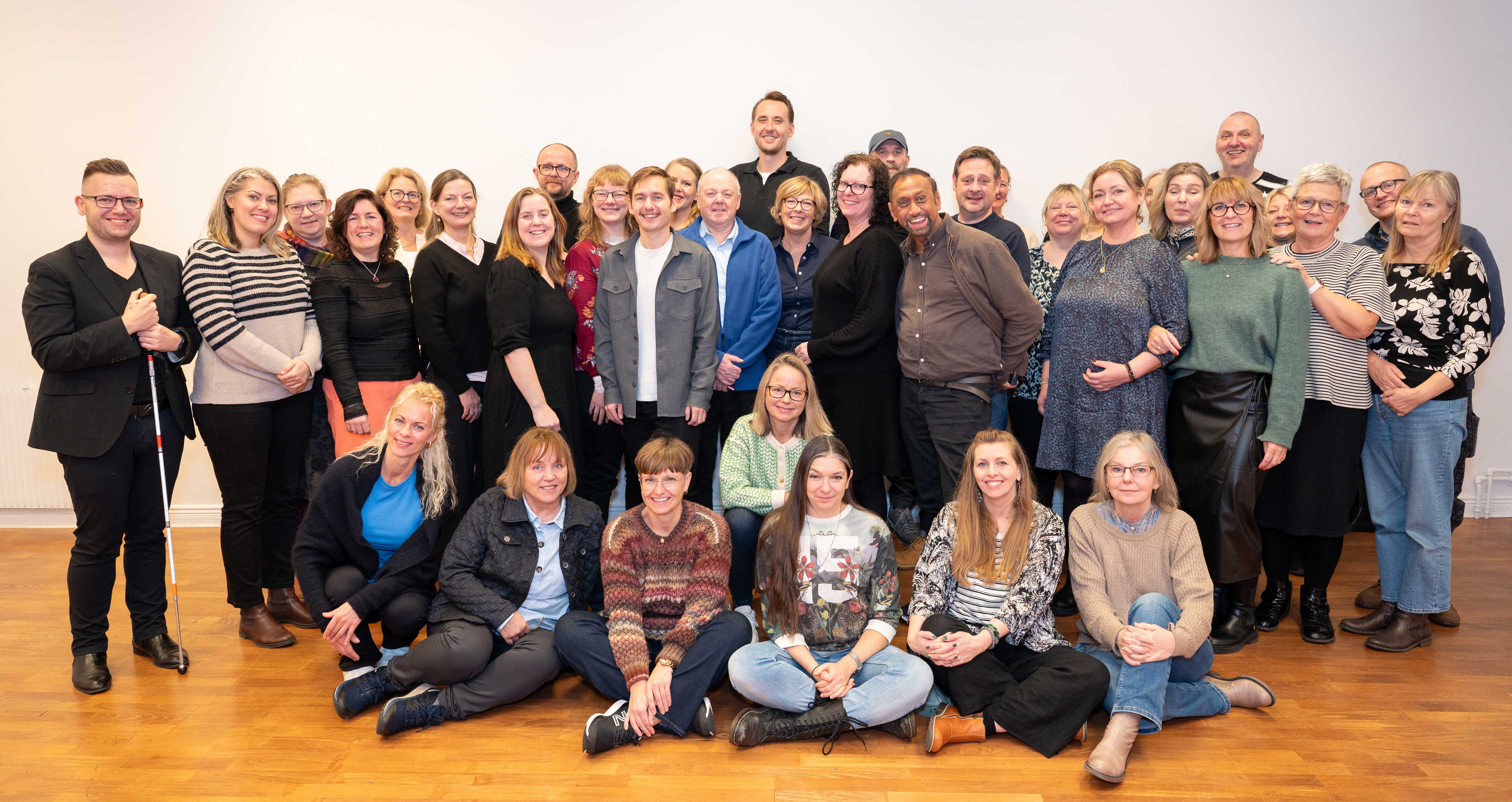 Group photo of around 35 people standing and sitting indoors, smiling at the camera.