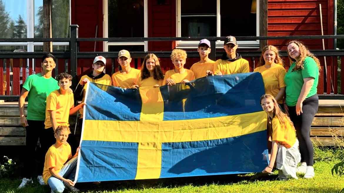 Smilende barn utendørs, og holder et stort svensk flagg.
