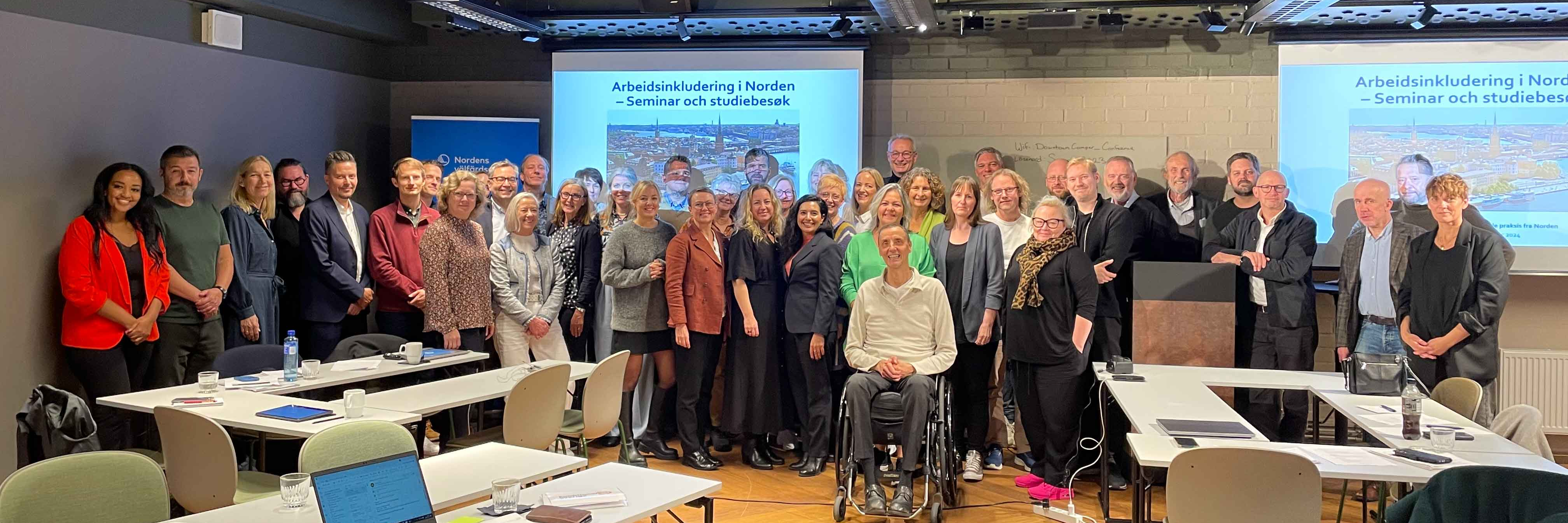 Ca. 35 personer på et gruppebilde i et konferanserom. Alle er kledd i kontorklær og ser fornøyde inn i kameraet. På bordene i forgrunnen står datamaskiner.    