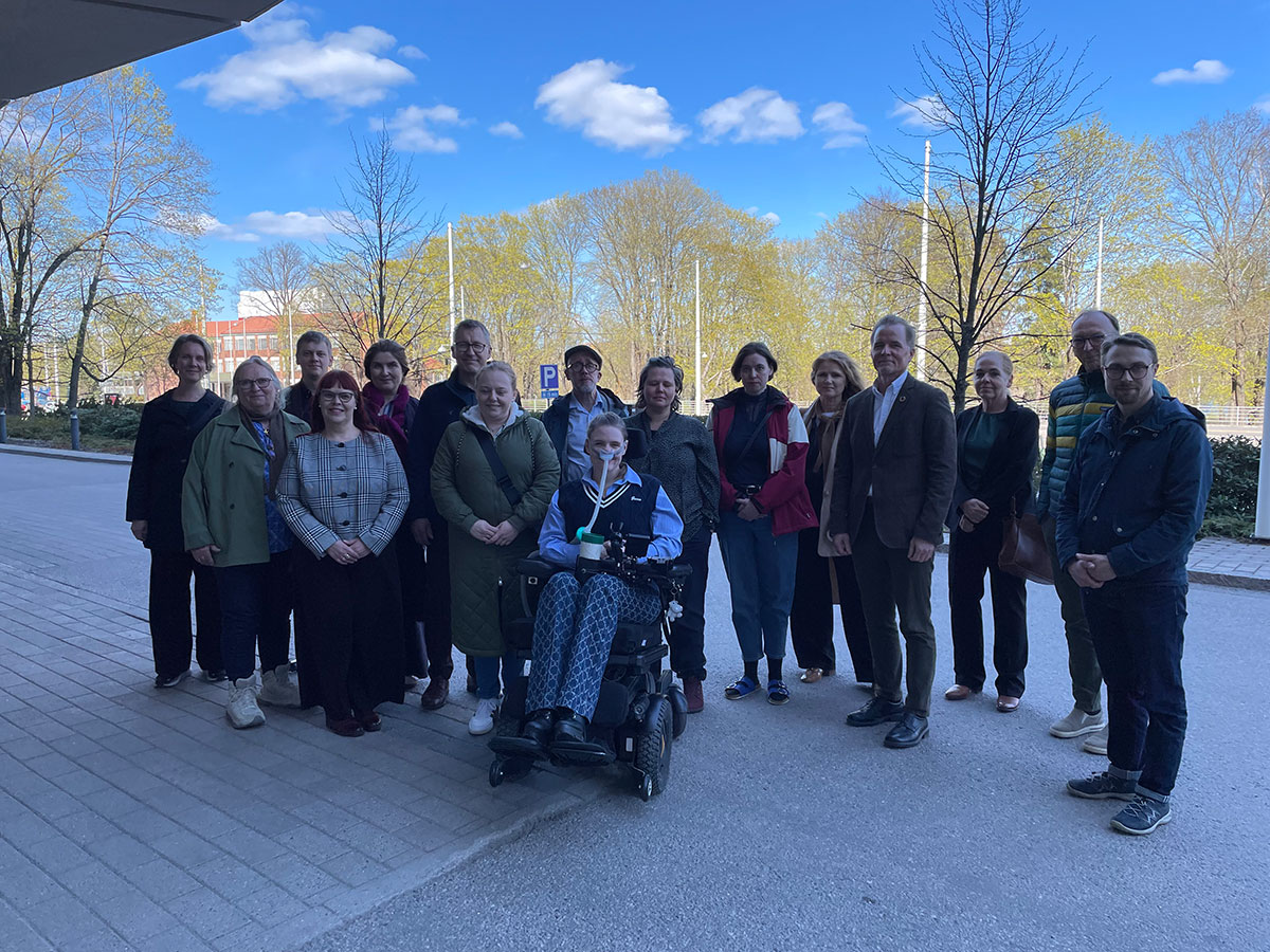16 personer som står eller sitter i rullestoler utendørs på et gruppebilde
