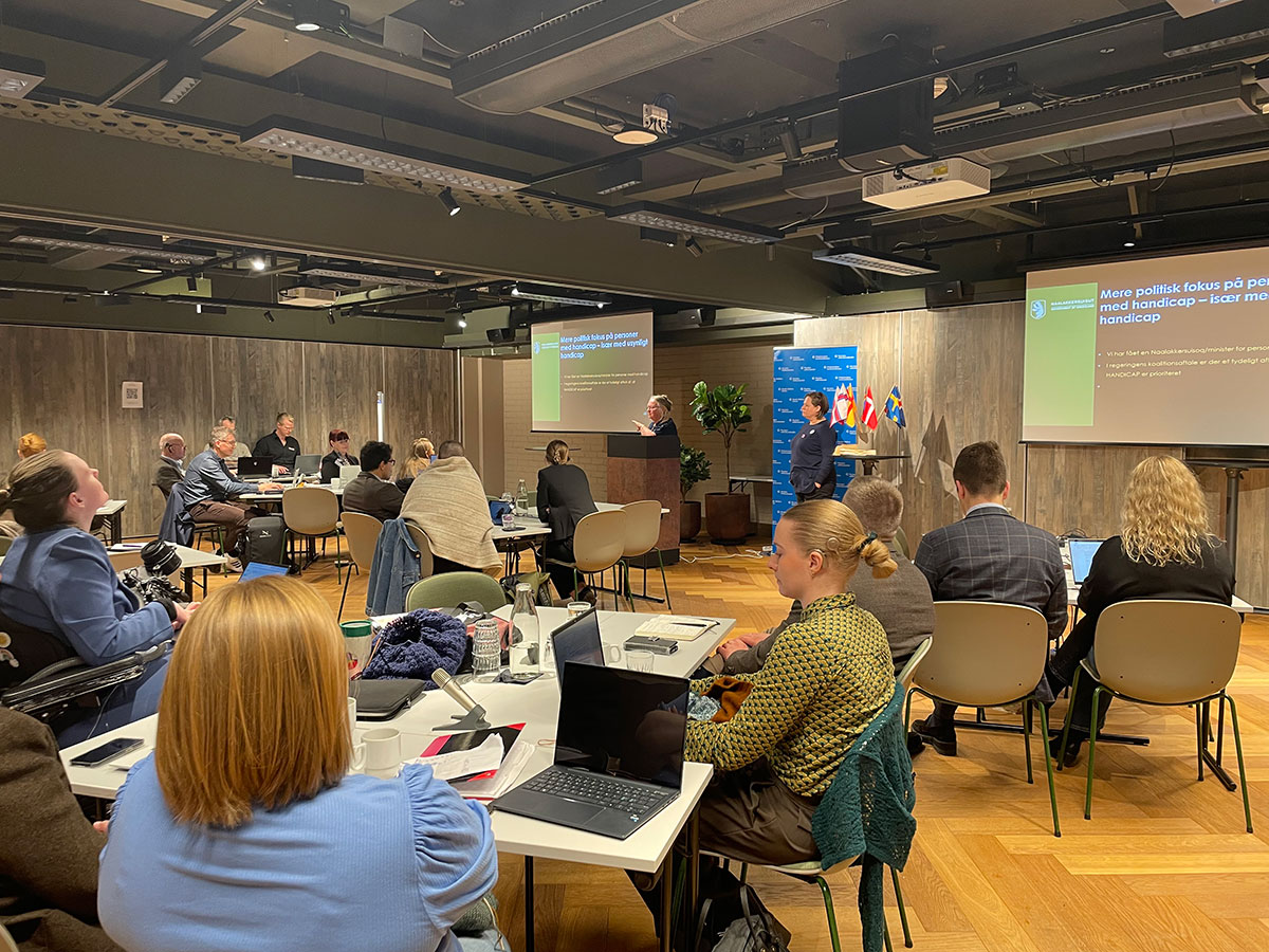 To personer holder en presentasjon i et konferanserom, mens mange andre lytter.