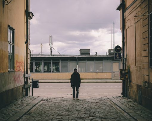 En ensam person står mellan två hus i Stockholm.