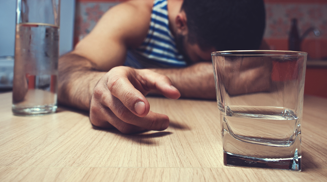 En person sträcker sig efter ett glas med starksprit.