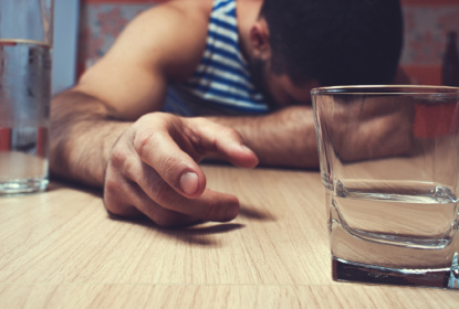En person sträcker sig efter ett glas med starksprit.