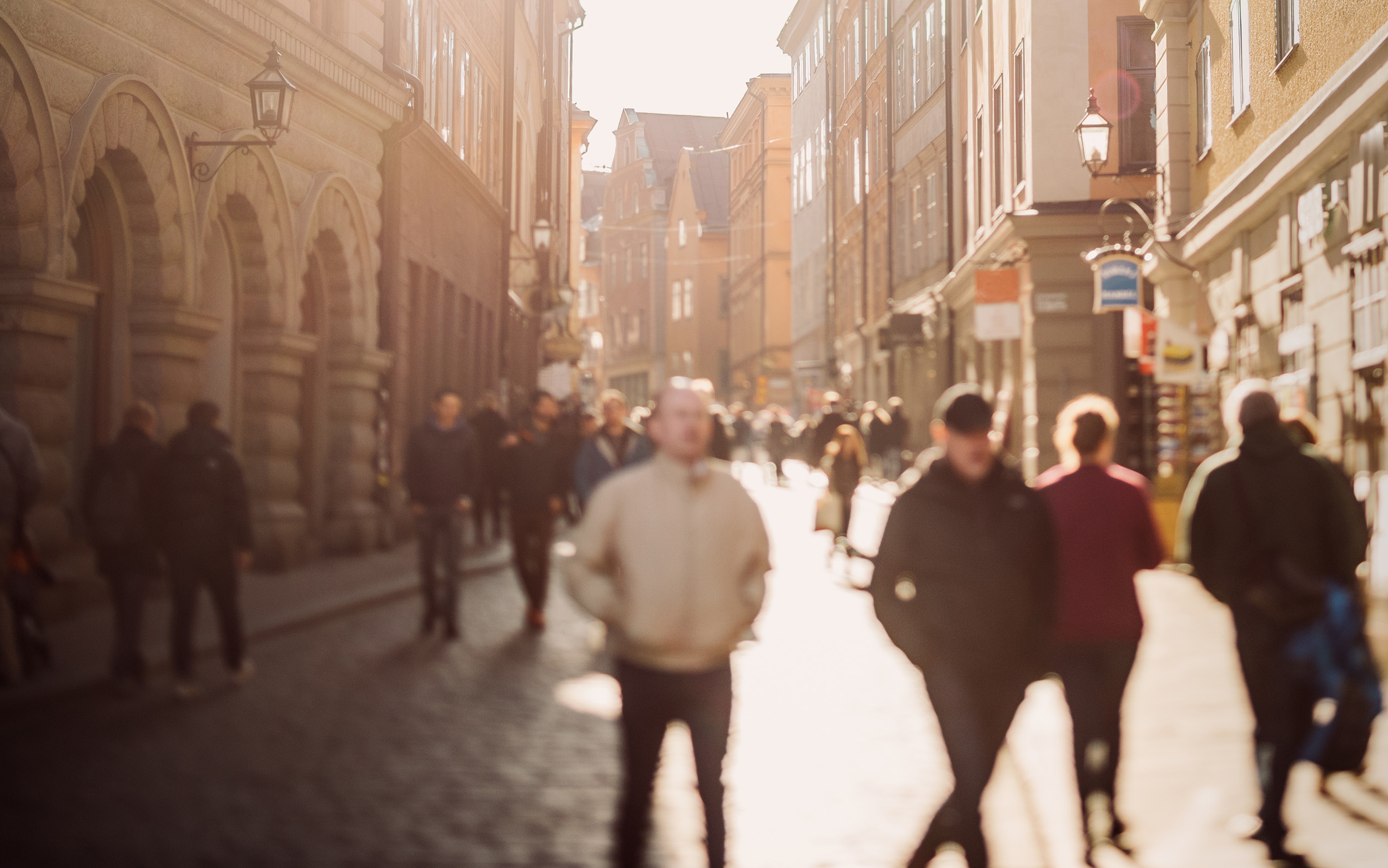 Personer som promenerar i sol på en gata i en stad.