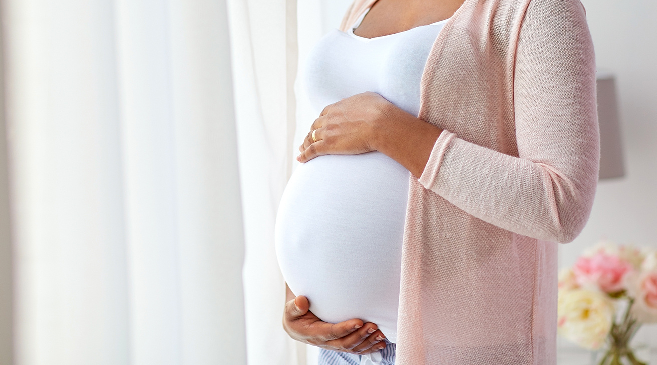 Gravid person håller händerna på magen.