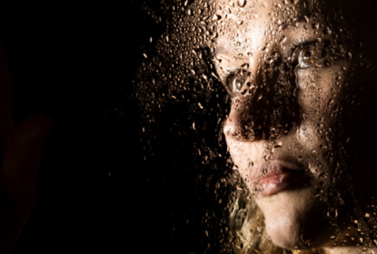 Smooth portrait of sexy model, posing behind transparent glass covered by water drops. young melancholy and sad woman portrait