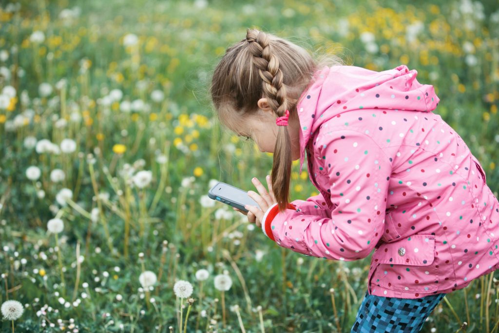 Flicka tar foton av blommor med sin mobil.