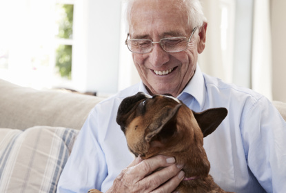 Pensionär sitter och klappar en hund.