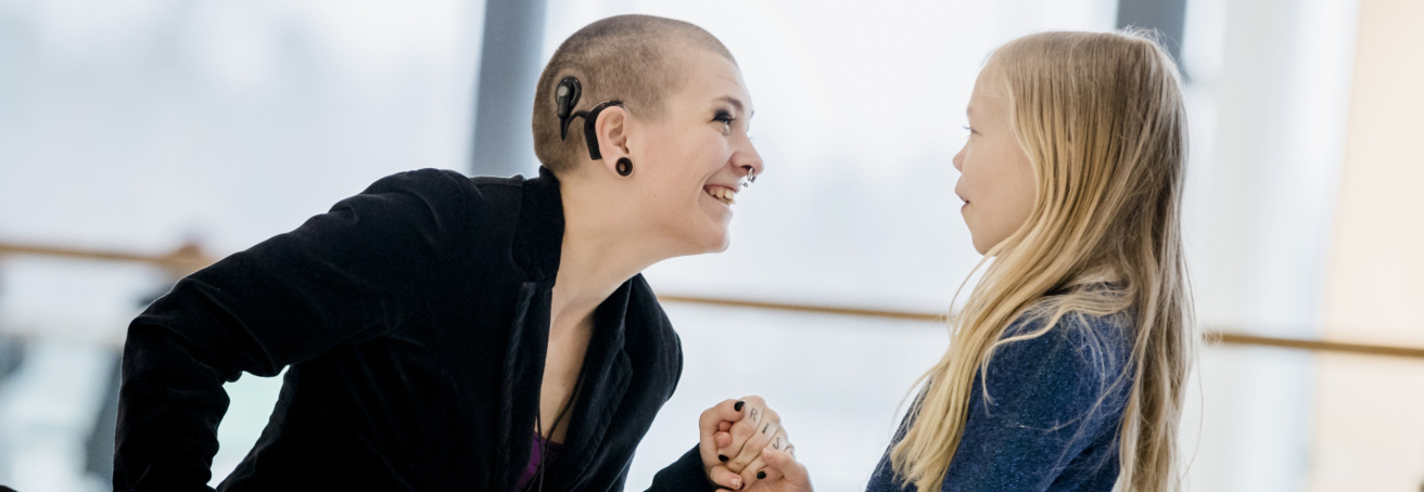 Kvinna med cochlear-implantat sitter i rullstol och skrattar med barn hon håller i handen