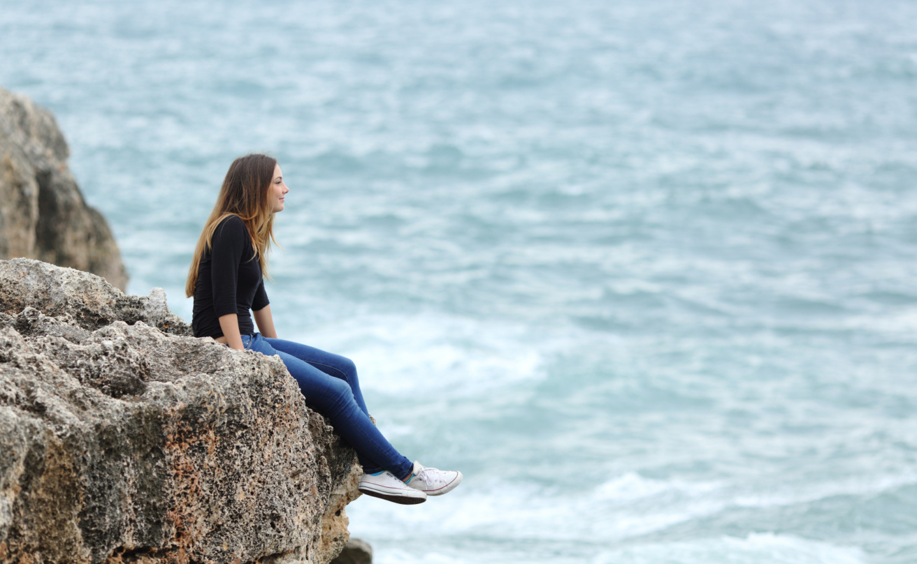 11328193-casual-woman-sitting-in-a-cliff-watching-the-sea