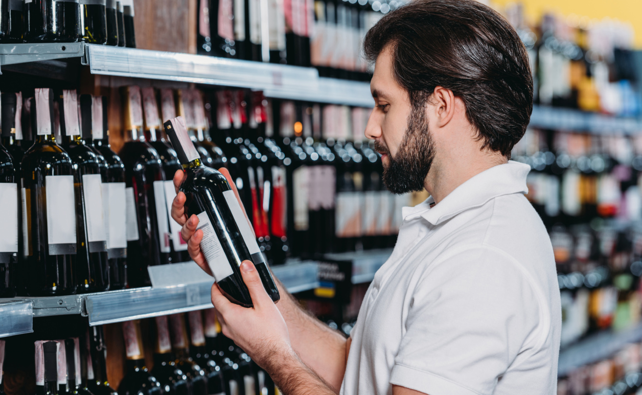 male shop assistant arranging alcohol in supermarket