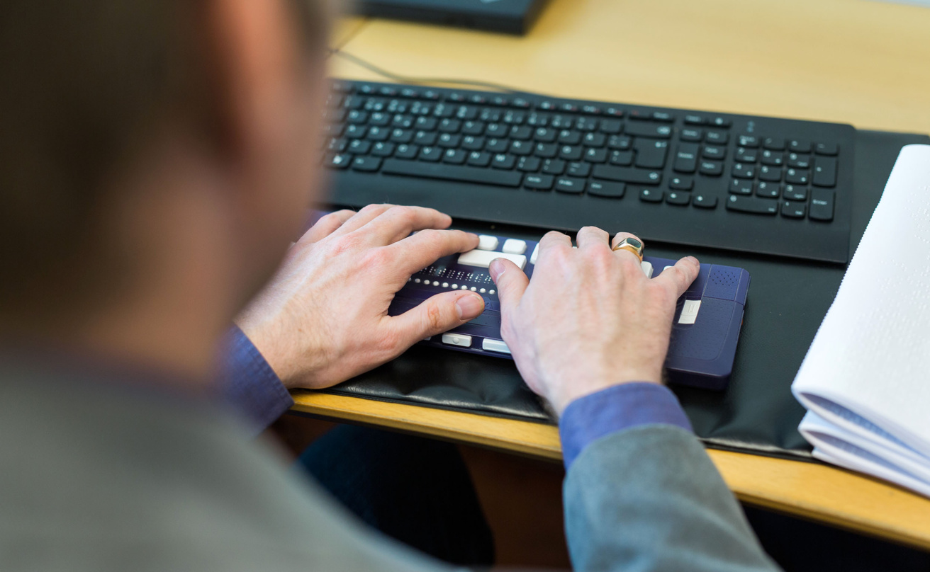 Man vid skrivbord skriver på tangentbord för personer med synnedsättning.