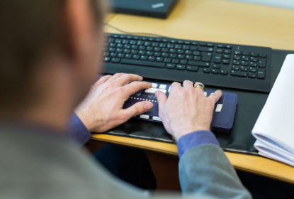 Man vid skrivbord skriver på tangentbord för personer med synnedsättning.