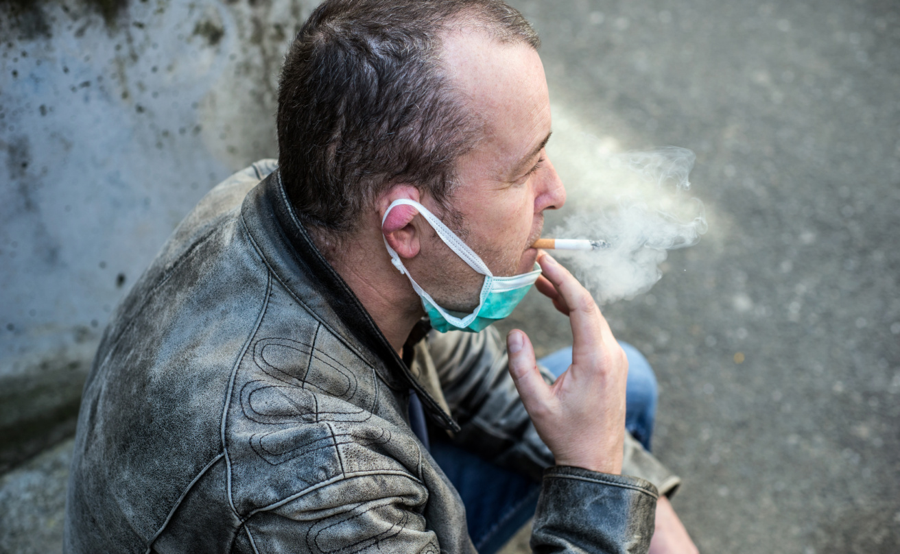 Portrait of caucasian man smoking a cigarette with a medical mask in the street during the covid-19 pandemic
