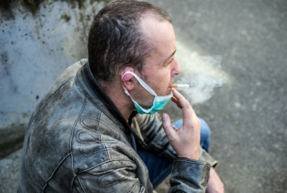 Portrait of caucasian man smoking a cigarette with a medical mask in the street during the covid-19 pandemic