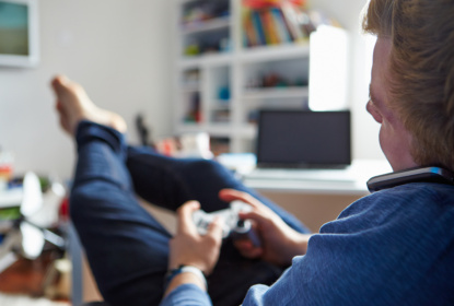 Teenage Boy Playing Video Game And Talking On Mobile Phone