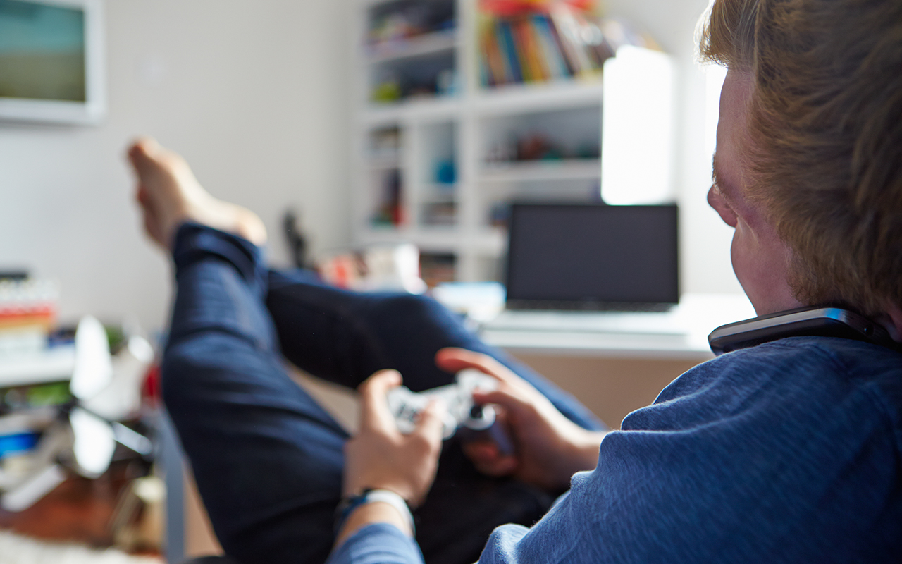 Teenage Boy Playing Video Game And Talking On Mobile Phone