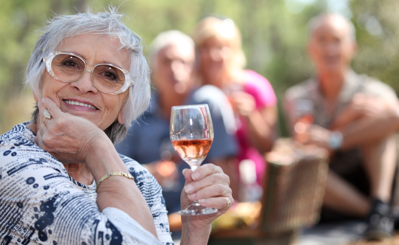 Äldre kvinna dricker ett glas vin tillsammans med vänner