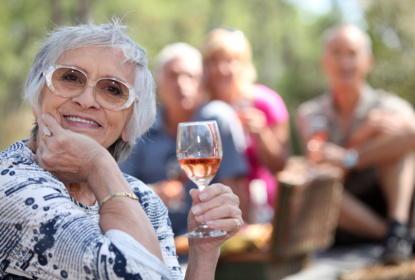 Äldre kvinna dricker ett glas vin tillsammans med vänner