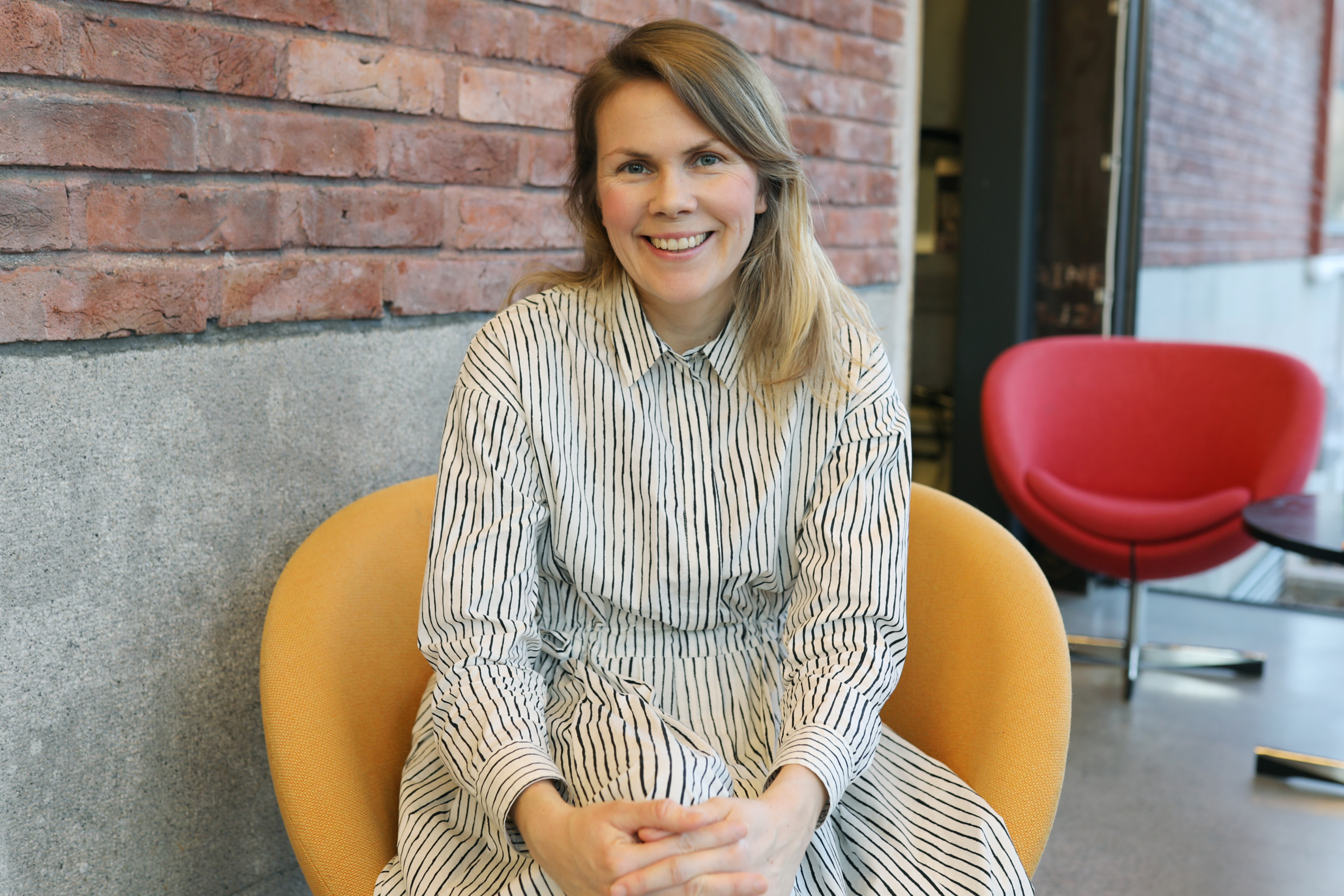 Porträtt av Malin Kock Hansen som har långt hår och sitter i en fåtölj