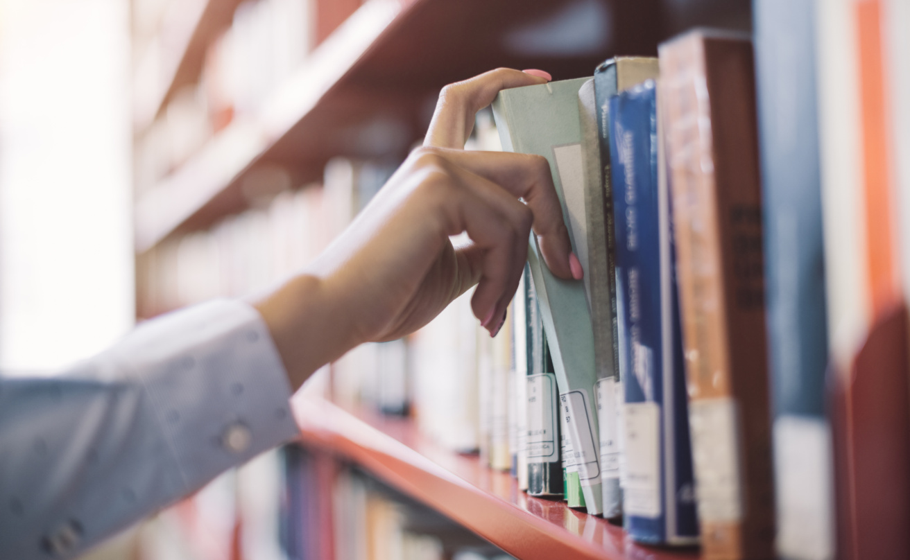 Bild av en hand som tar en bok ur en bibliotekshylla.