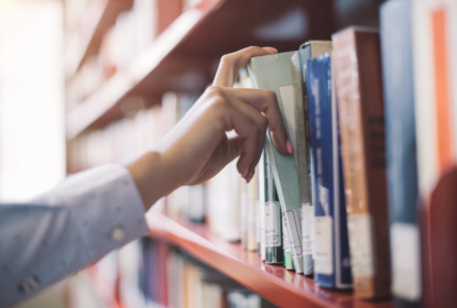 Bild av en hand som tar en bok ur en bibliotekshylla.