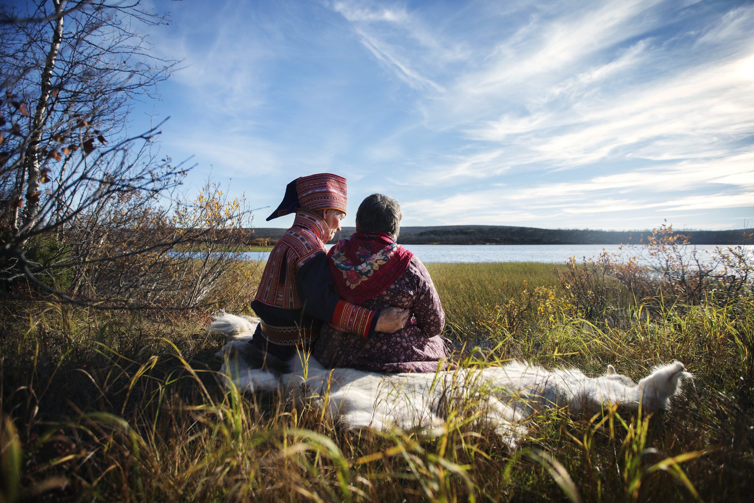 Samiskt äldre par sitter i naturen sedda bakifrån.