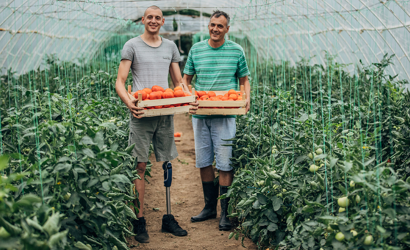 Two smiling men holding plants - one man with bone prosthesis