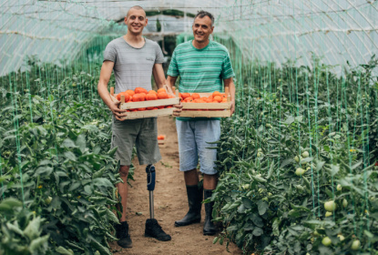 Two smiling men holding plants - one man with bone prosthesis