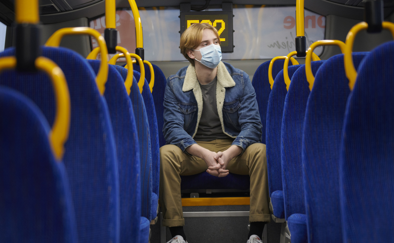 En kille sitter på en buss med munskydd.
