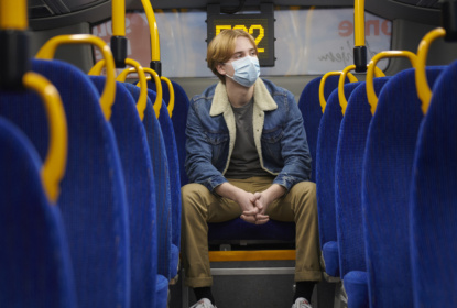 En kille sitter på en buss med munskydd.
