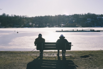 Två personer sitter på en parkbänk och tittar ut över vatten.