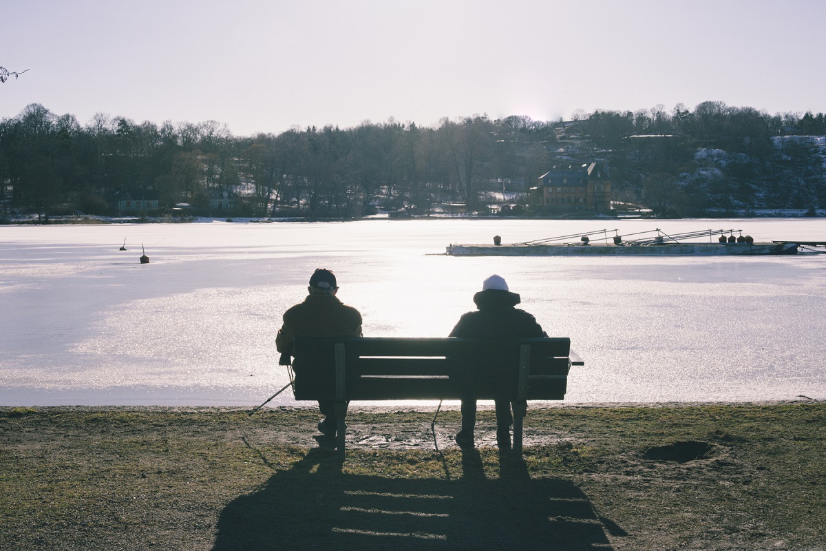 Två personer sitter på en parkbänk och tittar ut över vatten.