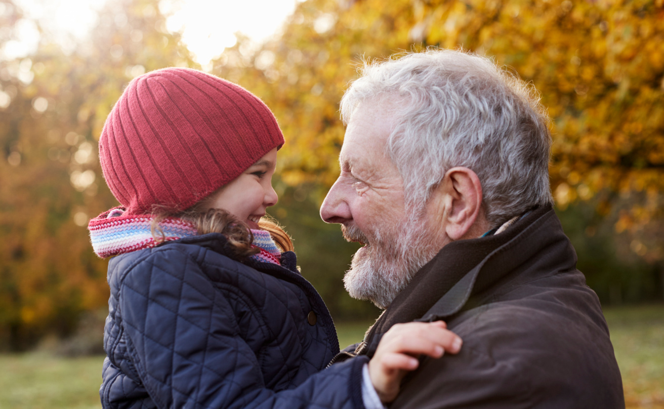 Grandfather cuddling granddaughter on autumn walk