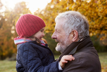 Grandfather cuddling granddaughter on autumn walk