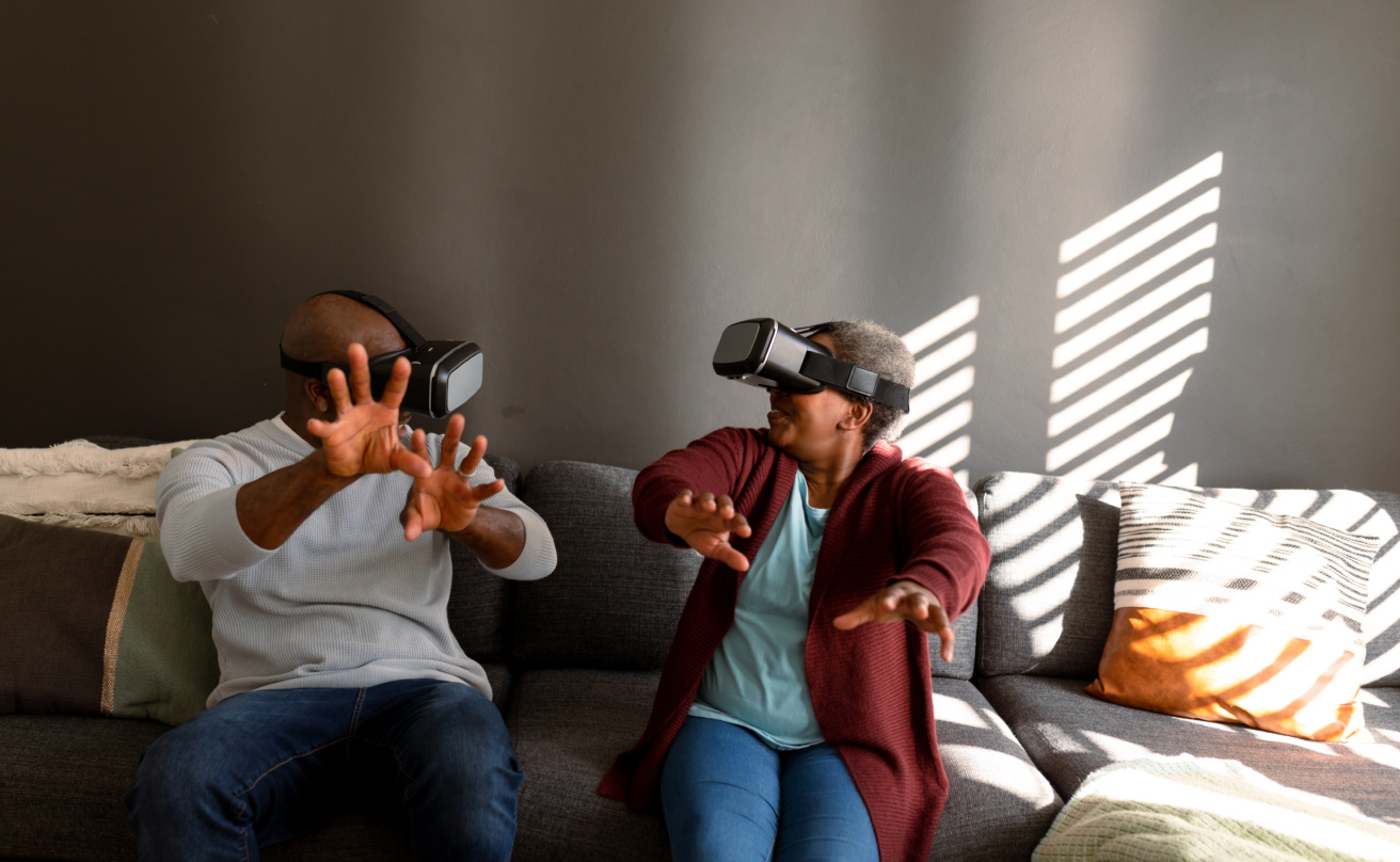 Äldre man och kvinna sitter i en soffa och spelar med VR-glasögon.