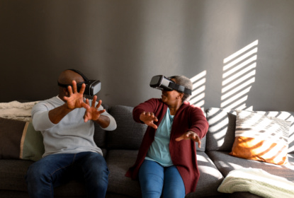 Äldre man och kvinna sitter i en soffa och spelar med VR-glasögon.