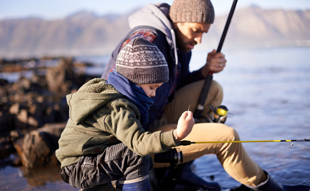 Little boy fishing with father side by side down by a lake