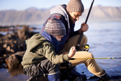Little boy fishing with father side by side down by a lake