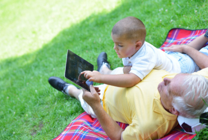 Grandfather and child looking at an ipad while both lying on green grass