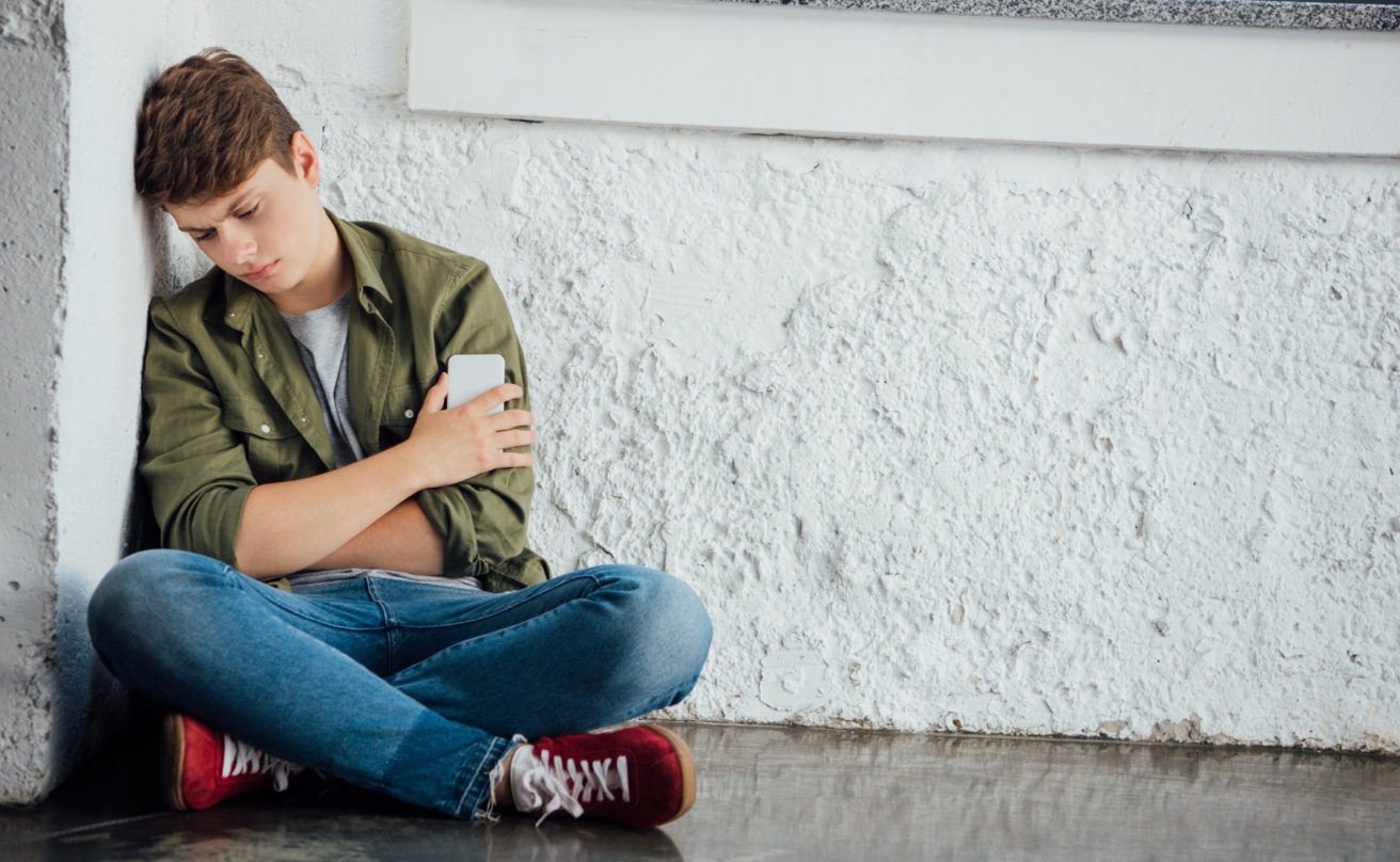 sad teenager sitting with crossed legs and holding phone