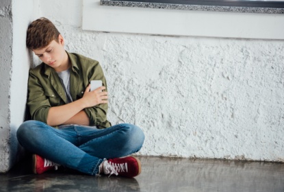 sad teenager sitting with crossed legs and holding phone