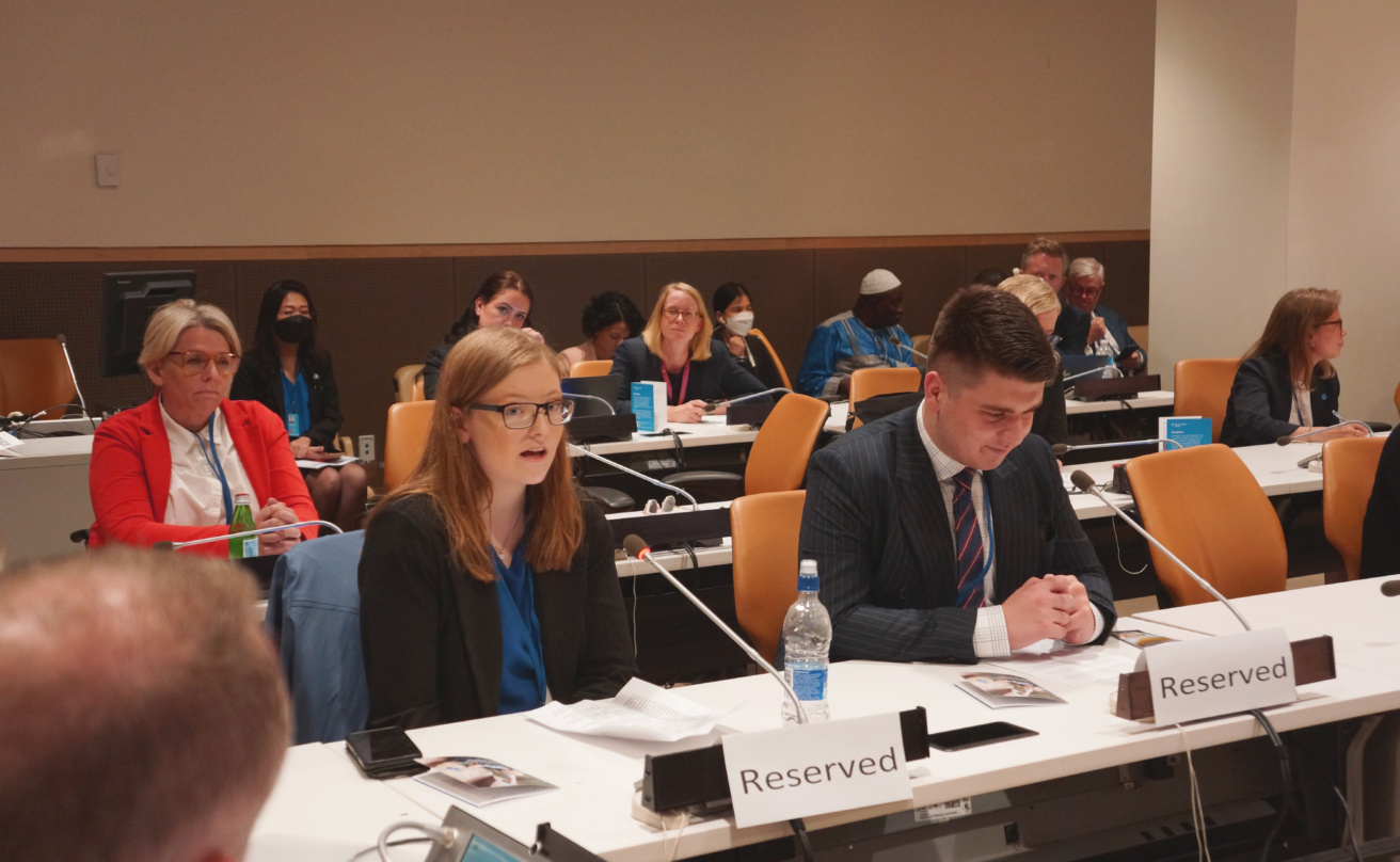 A woman and a man sitting at a conference table, the woman speaking