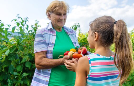 Mormor i trädgården med ett barn och en skörd av grönsaker.