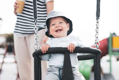 small child in a safe swing laughing and showing two teeth with a healthy start in life