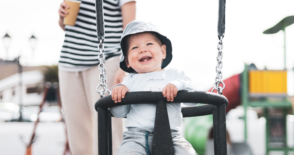 small child in a safe swing laughing and showing two teeth with a healthy start in life