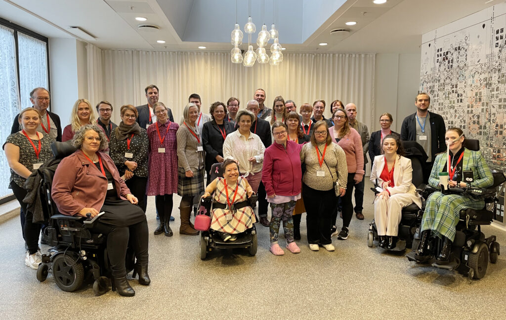 Group picture of 30 people standing and sitting in wheelchairs, inside a hotel lobby